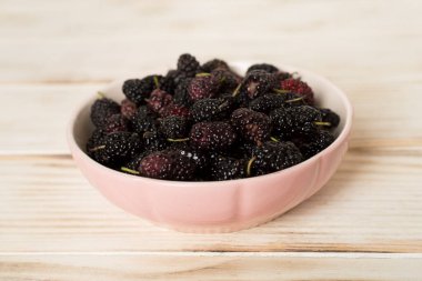 Bowls with mulberry fruit on wooden table.