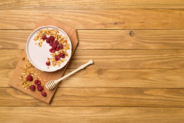 Bowl with granola, yogurt and fresh berries on wooden background, top view.