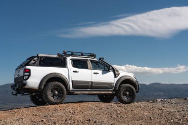 Custom made 4x4 white Ford pickup on the deserted road in the high mountains on the blue sky background.