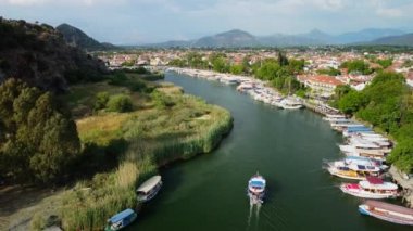 Yaz boyunca Dalyan nehrinde renkli tekneler. Arka planda Dalyan kasabası, bir sürü kırmızı çatı binaları, dağ manzarası, Türk manzarası..