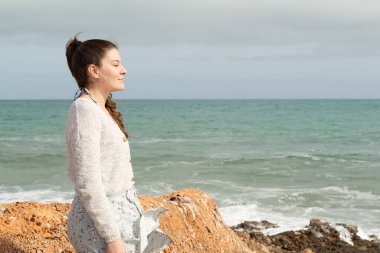 Gülümseyen kadın baharın bulutlu ve rüzgarlı bir gününde kıyıda durup güneşin tadını çıkarıyor.. 