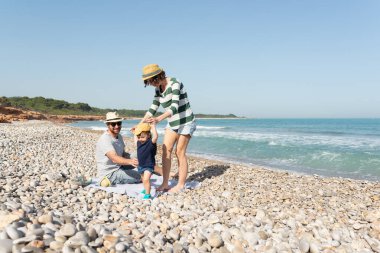 Anne, küçük kızına ilk adımlarında yardım ederken baba onlara Akdeniz sahilinde bakıyor.. 