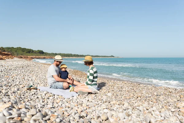 Baba, anne ve küçük kızları Akdeniz kıyısındaki çakıl taşı plajında oturuyorlar. Rahatlatıcı ve huzurlu tatiller.