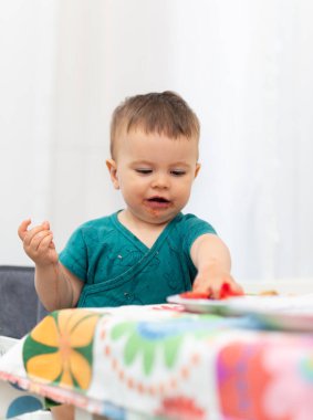Tek başına yemek yemeyi öğrenen 11 aylık mutlu bir bebek. Bir parça domates topluyor ve ortalığı kirletiyor..