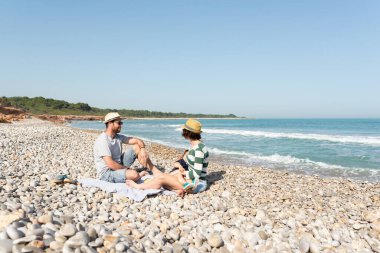 Akdeniz sahilinde oturan bir aile. Anne bebeğini besliyor. Dışarıda emziriyorlar..