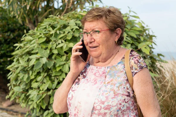 Half body portrait of a smiling senior woman talking on mobile phone on a park.