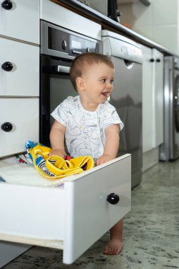 Pijamalı gülümseyen kız mutfaktaki çekmeceden bir şeyler çıkarıyor. Evini keşfeden bebek. 