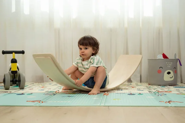 Toddler wobbling on a balance board in her playroom.