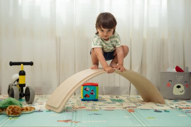 Montessori oyun odasındaki denge tahtasındaki kameraya bakan çocuk..