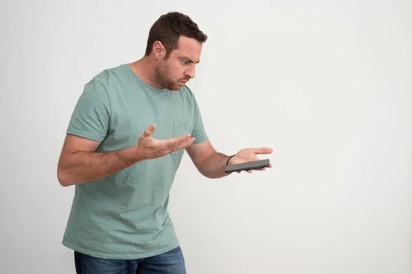 Isolated man with a sad expression is looking at smartphone, which he holds in one hand and points with the palm of the other hand. Upset and sad man after a phone call.