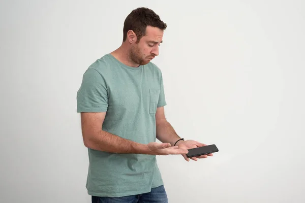 Isolated man with a sad expression is looking at smartphone, which he holds in one hand and points with the palm of the other hand. Upset and sad man after a phone call.