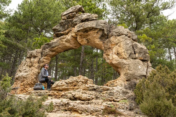 Man contemplating a natural stone arch while is resting during a trekking. Active vacations. 