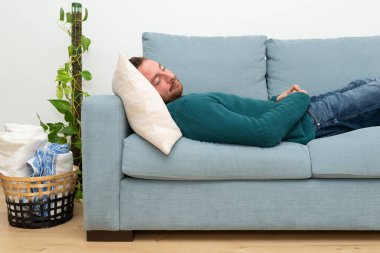 Attractive and bearded man sleeping on a blue sofa in his modern apartment. Resting time.