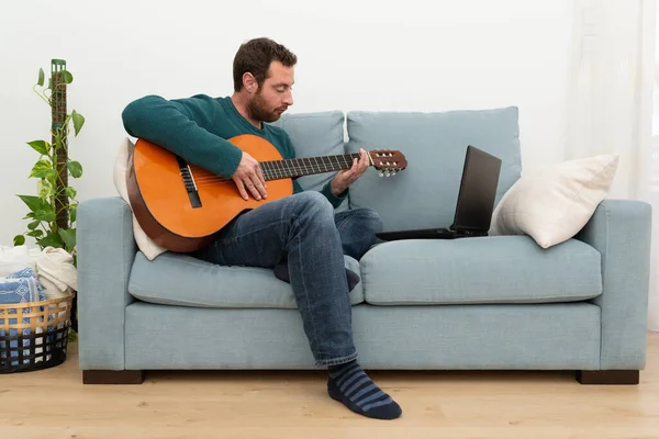 Young man sitting in his sofa attending a spanish guitar online class.