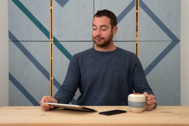 Çekici bir işadamı elinde bir fincan kahve tutarken tabletten bazı raporlar okuyor..