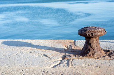 Güneşli bir günde arka planında mavi okyanus olan taştan bir rıhtımda Rusty Bollard. Denizcilik kavramı.