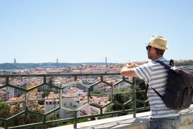 Yazlık şapkalı ve sırt çantalı bir adam Lizbon 'dan manzaranın tadını çıkarıyor. Gezmek ve gezmek.