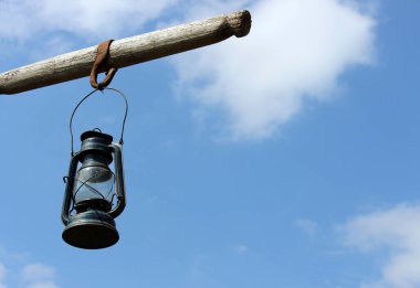 Arka planda açık mavi gökyüzü olan tahta bir direkte antik bir fener.