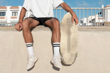 Tanımlanamayan kaykaycı, kaykay rampasının kenarında oturuyor. Yazlık giysiler giyiyor..