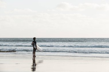 Gün batımında sahilde dalgaları seyreden sörfçü.