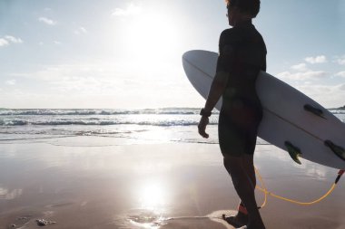 Genç sörfçü sahilde dalgaları seyrediyor.