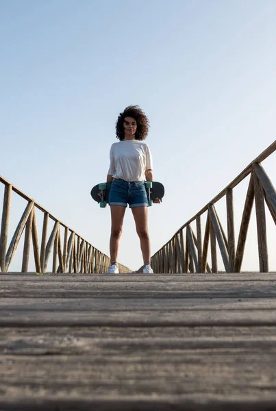Genç patenci, afro saçlı, dışarıda duran kaykayını tutan kadın.