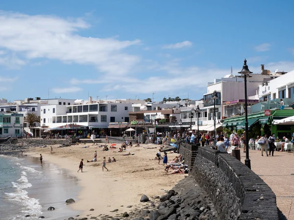Playa Blanca, İspanya; 26 Mart 2022: Playa Blanca, Lanzarote 'deki turistik kasaba. Turistler kumsalda güneşleniyor ve gezinti güvertesinde yürüyor.