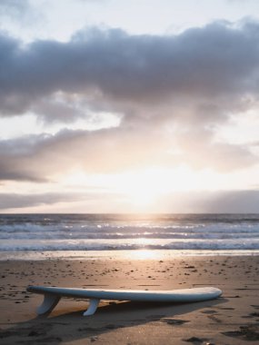 Surfboard lying on the beach and the sunrise in a cloudy sky