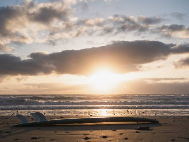 A surfboard lying on the beach shore and sunrise over the ocean waves