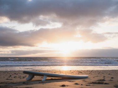 Surfboard lying on the beach at sunrise under a cloudy sky