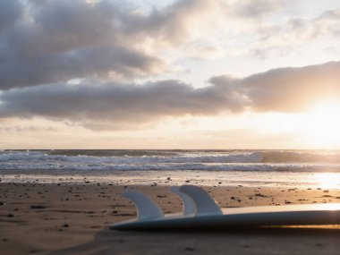 Morning waves at sunrise and a surfboard lying on the beach