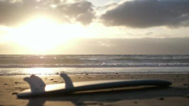 A surfboard lying on the beach shore at cloudy sunrise