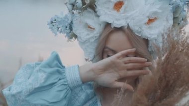 Kafasında çelenk olan Ukrayna vatandaşı bir kadın. Nakış. Nakış. Nehir manzarası. Elinde sarı çimen olan bir kadın.