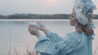 Kafasında çelenk olan Ukrayna vatandaşı bir kadın. Nakış. Nakış. Nehir manzarası. Elinde kağıt bir tekne tutan bir kadın.