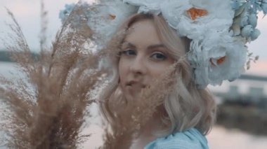 Kafasında çelenk olan Ukrayna vatandaşı bir kadın. Nakış. Nakış. Nehir manzarası. Elinde sarı çimen olan bir kadın. Yavaş çekim