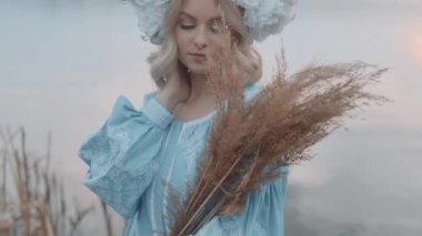 Kafasında çelenk olan Ukrayna vatandaşı bir kadın. Nakış. Nakış. Nehir manzarası. Elinde sarı çimen olan bir kadın. Yavaş çekim