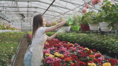 Girl sprays flowers in the garden. Caucasian woman takes care of plants by moisturizing them. Slow motion video of gardening