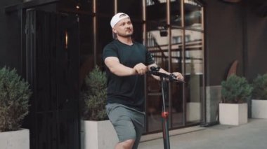 Young man standing with e-scooter in city downtown and taking selfie with smartphone