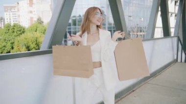 Sexy smiling woman in white suit walks with shoping bags in the city urban street. Steadicam stabilized shot in Slow motion