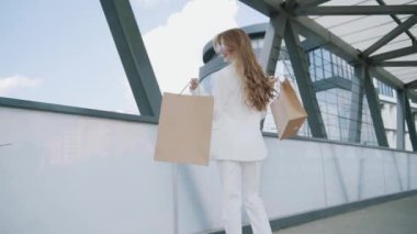 Sexy smiling woman in white suit walks with shoping bags in the city urban street. Steadicam stabilized shot in Slow motion