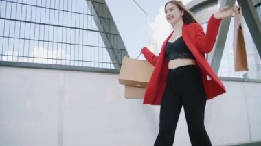 Sexy smiling woman in red jacket walks with shoping bags in the city urban street