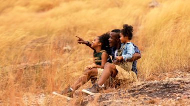 Mutlu Afrikalı aile babası ve kızı seyahat ediyor ve gölgede çayırlık doğayı işaret ederek gün batımını seyrediyor. Seyahat ve Aile Konsepti