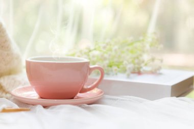 Kahve sabahı. Rahatlamak için pembe buharlı kahve. Hobilerini yaptıktan sonra çiçeklerle dolu beyaz tahta bir pencereye tığ işi yapıyor.. 