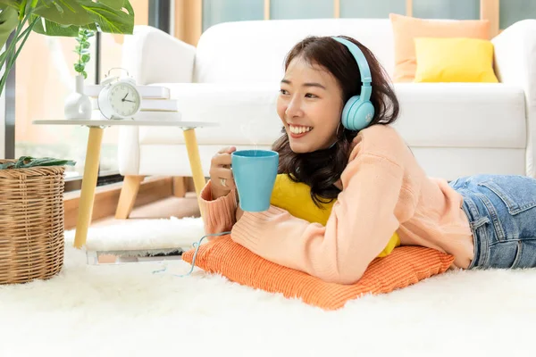 Home lifestyle woman relaxing lying down in living room. Happy girl shopping and listen music on laptop for wellness and health in weekend holiday.  Lifestyle Concept