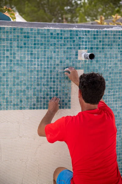 Worker repairing the pool, laying turquoise-coloured gresite tiles - pool repairs