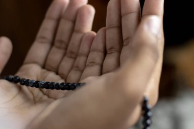 Genç Müslüman kadın Tasbeeh 'le namaz kılıyor. Arka plan Bulanık, Kapalı Alan. Ellere odaklan..