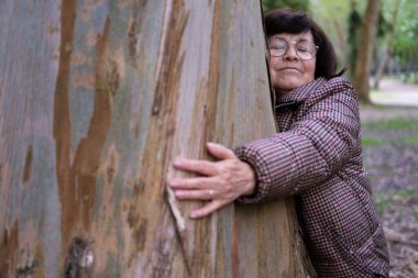 Ormanda büyük bir ağaca sarılan gözlüklü mutlu bir son sınıf öğrencisi.