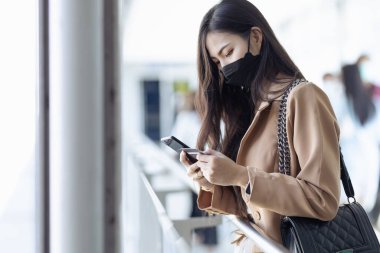 Asyalı kadın asansörle yukarı çıkıyor ve alışveriş merkezinden alışveriş yapmak için cep telefonuyla oynuyor..