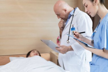 Doktor ve tıp öğrencisi yatakta yatan hastayı muayene ediyor.