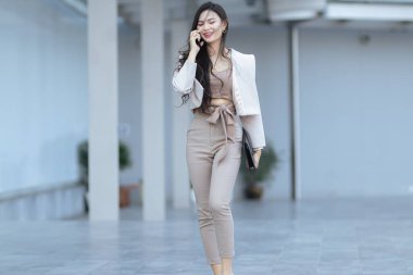 Asyalı iş kadını elinde dizüstü bilgisayarla telefonda yürüyor.